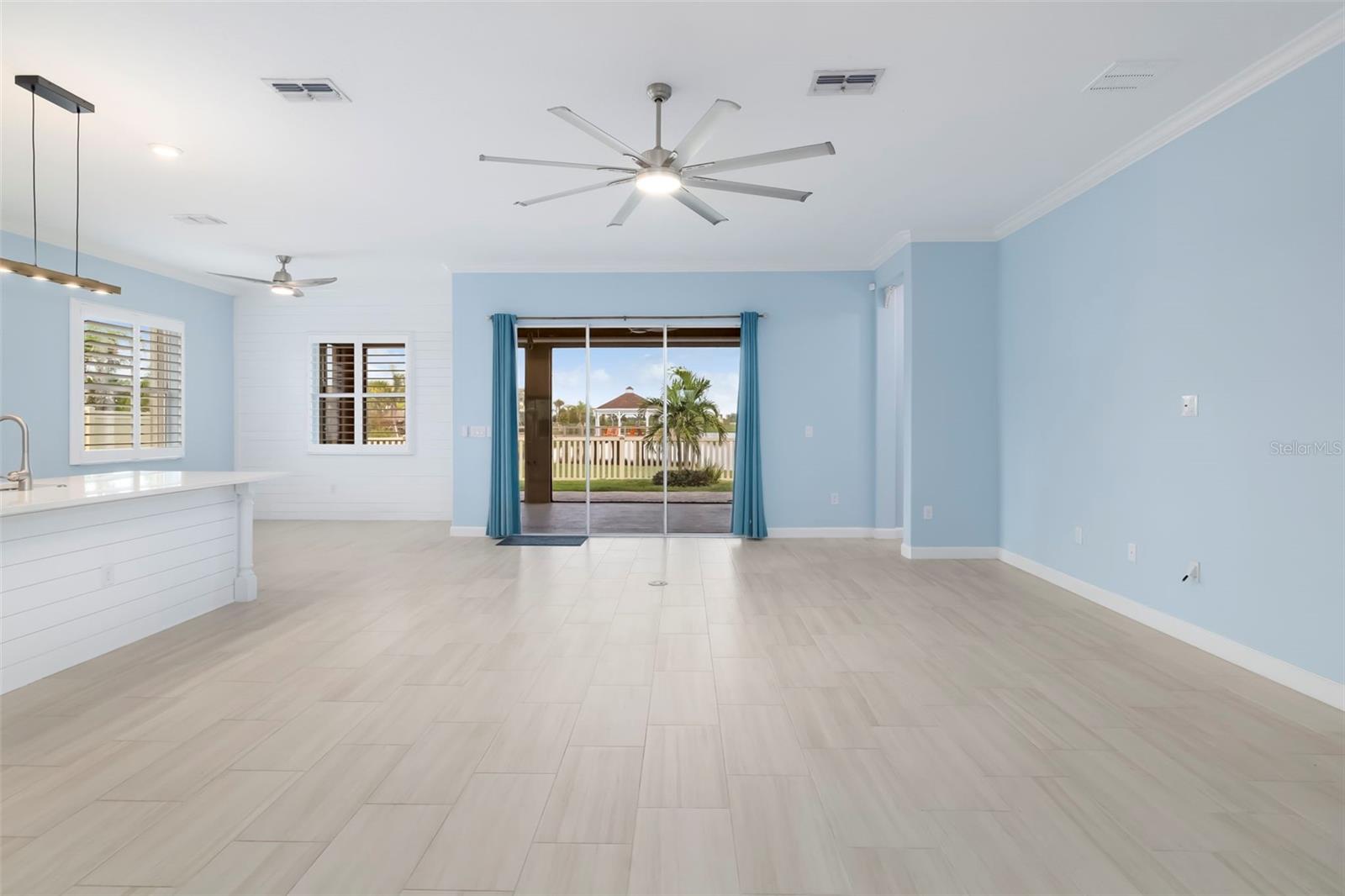 Open-plan living area with pale tile floors, blue walls, and sliding doors to the yard.