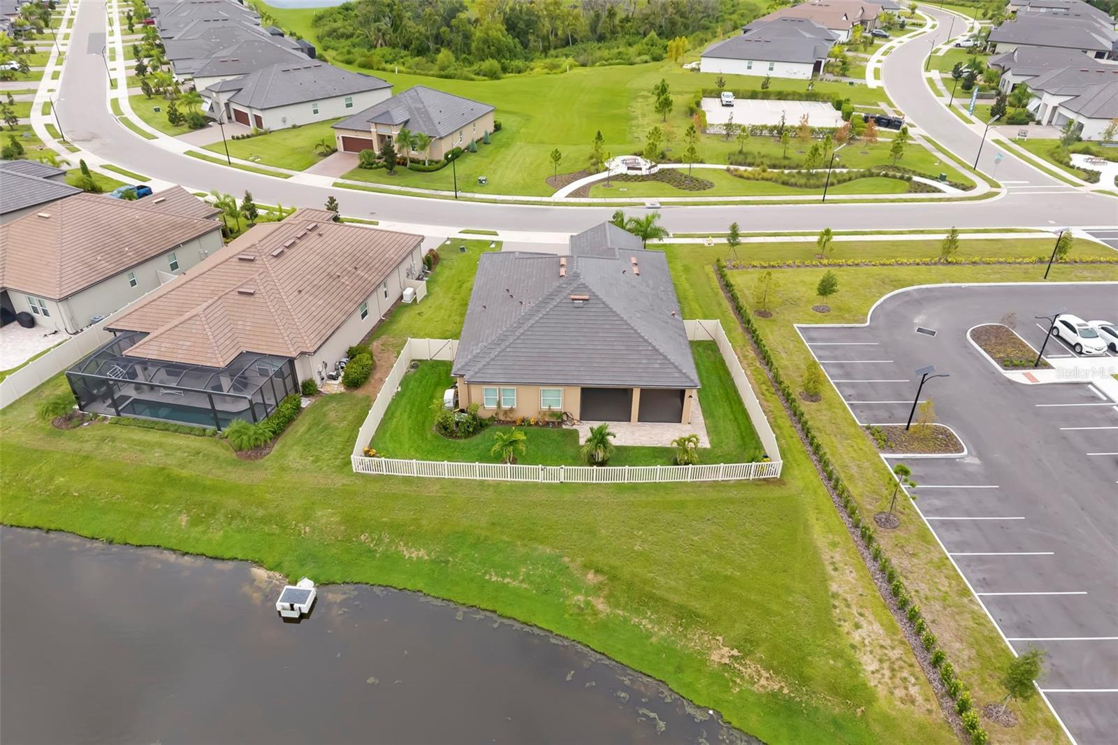 Aerial view of a home beside a pond, with a fenced lawn and neighboring houses.