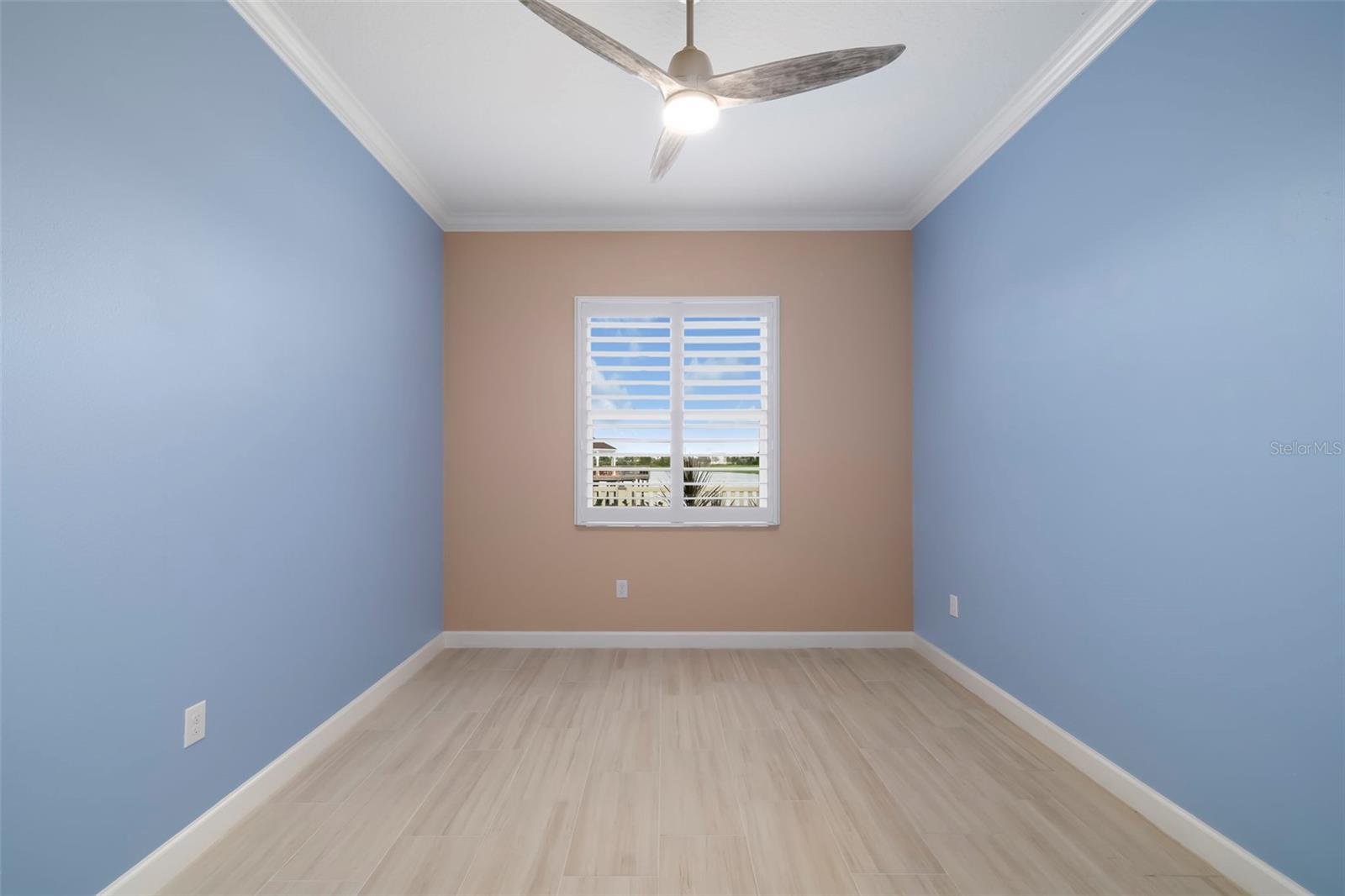 Empty bedroom with pale blue walls, tan accent wall, shuttered window, and ceiling fan.