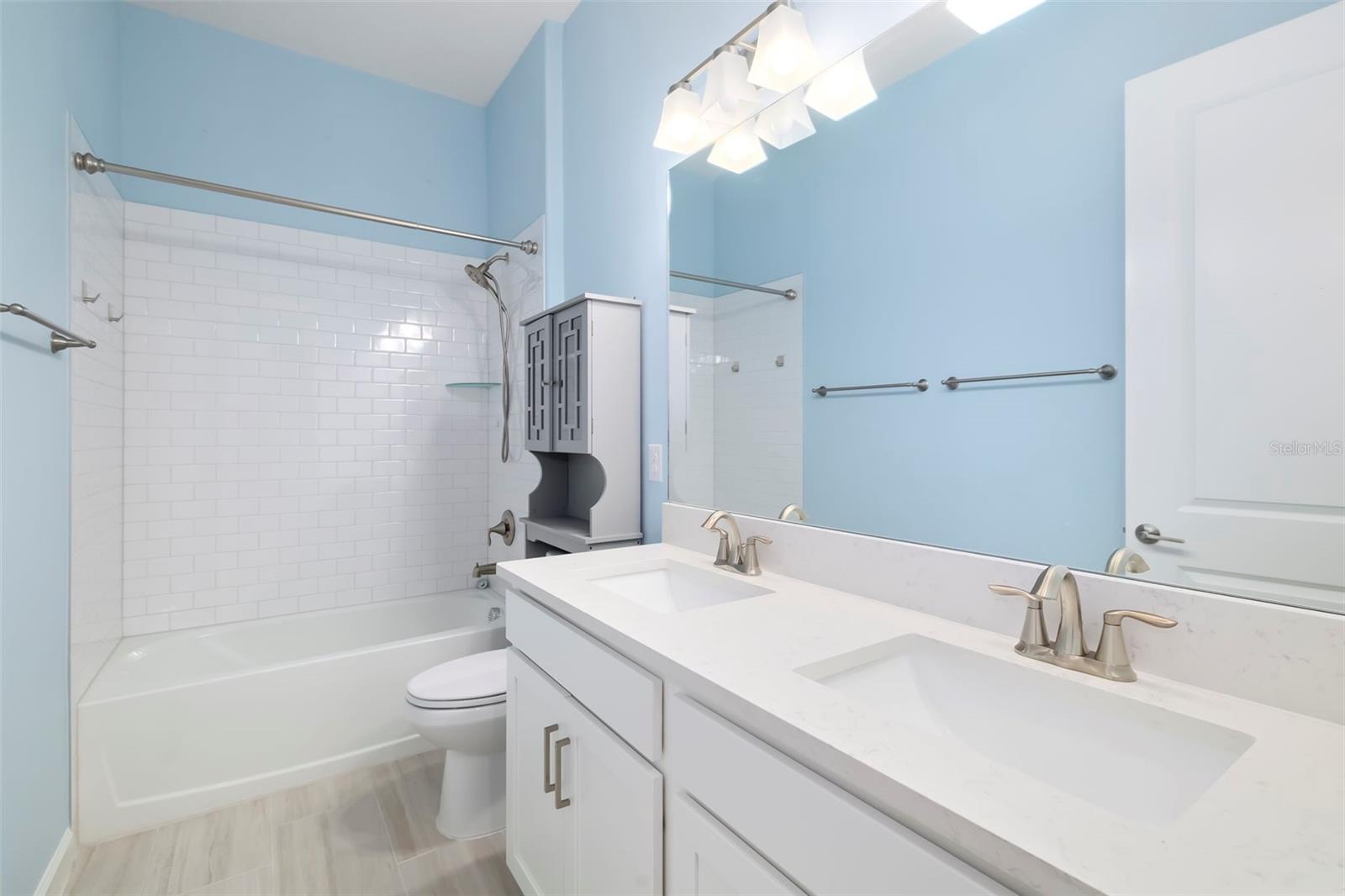 Bathroom with a white double vanity and mirror beside a subway-tile tub and shower.
