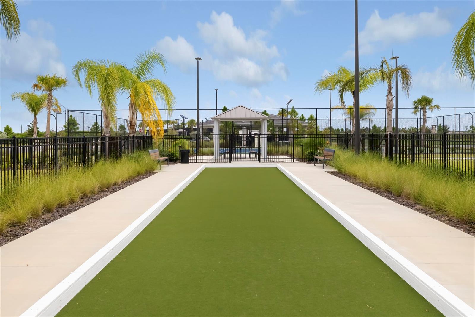 Outdoor green recreation court with white borders, benches, palm trees, and a pavilion.