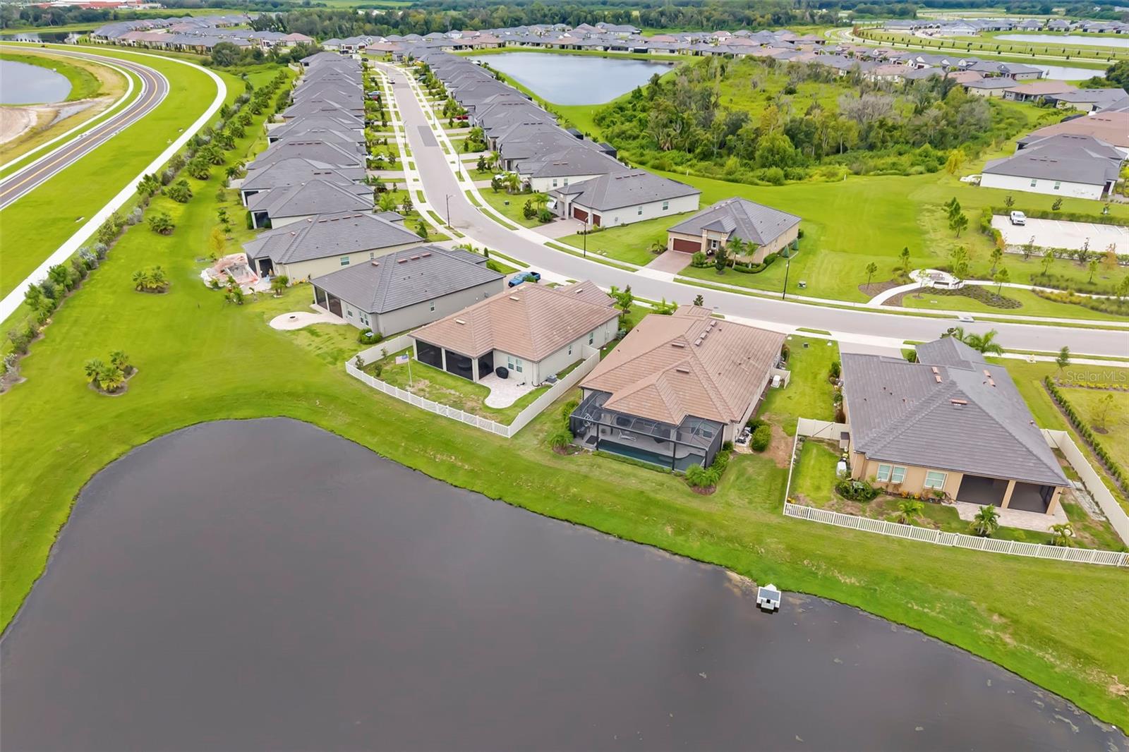 Aerial view of homes along a pond in a landscaped residential neighborhood.