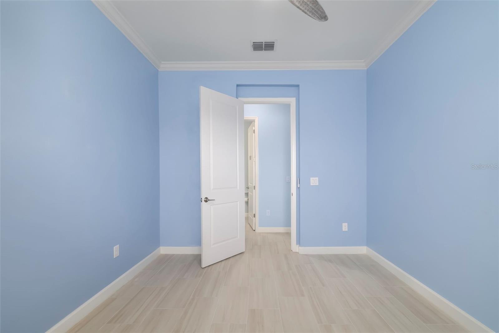 Empty blue-walled room with pale tile flooring and an open door.