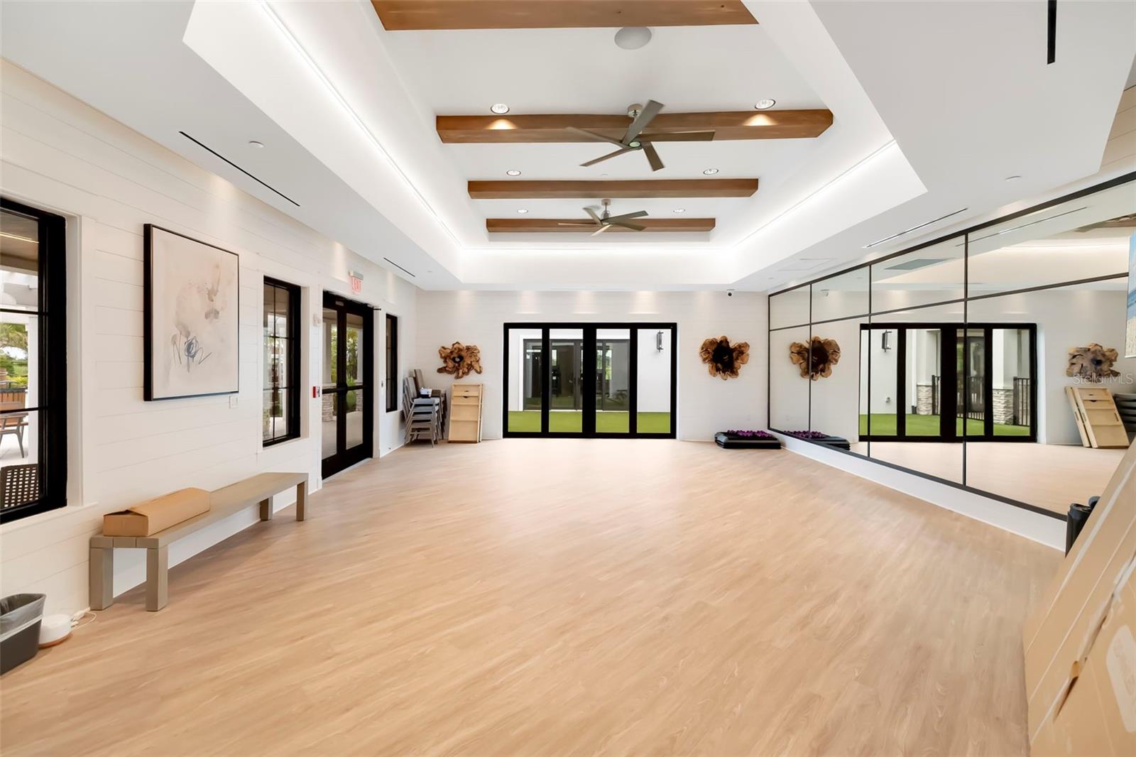 Bright exercise studio with mirrored wall, light wood flooring, and wood ceiling accents.