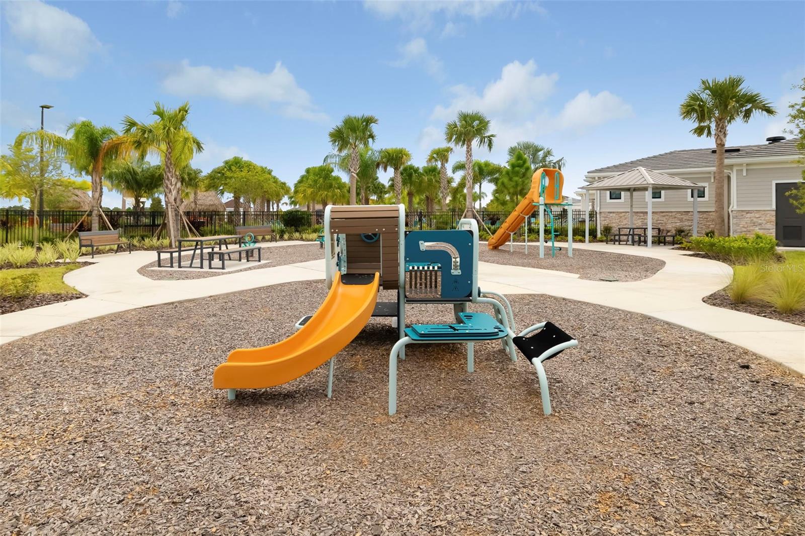 Community playground with orange slides, benches, palm trees, and a shaded pavilion.