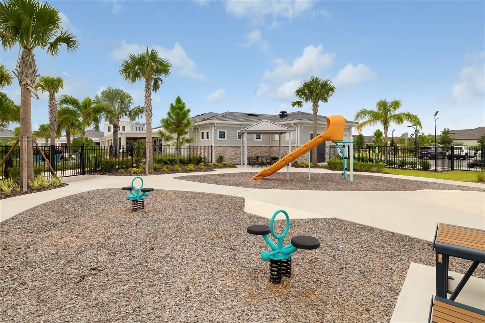 Community playground with an orange slide, turquoise spring riders, palm trees, and a clubhouse.