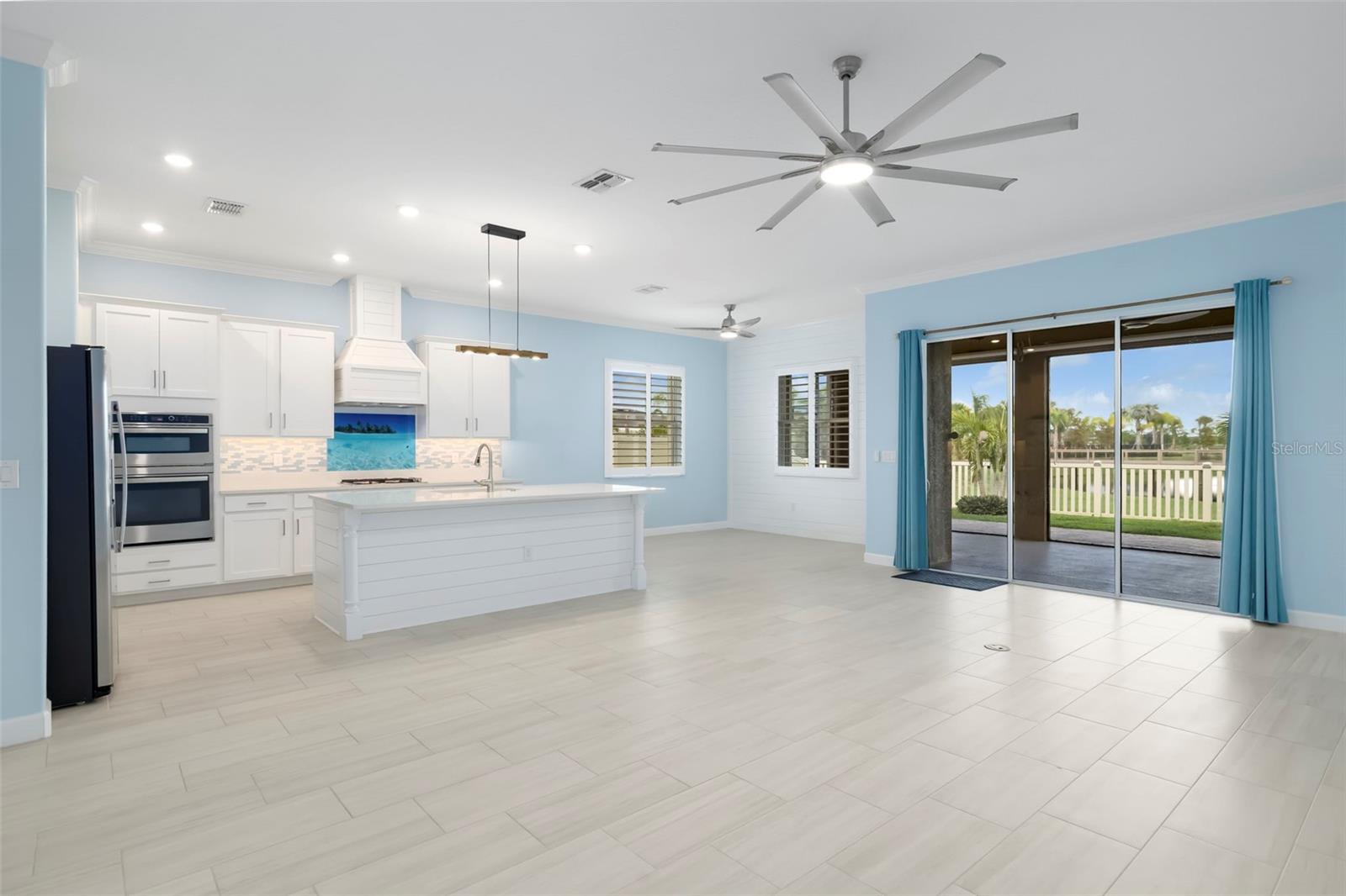 Open kitchen with a white island and blue walls, opening through sliding doors to a fenced waterfront yard.