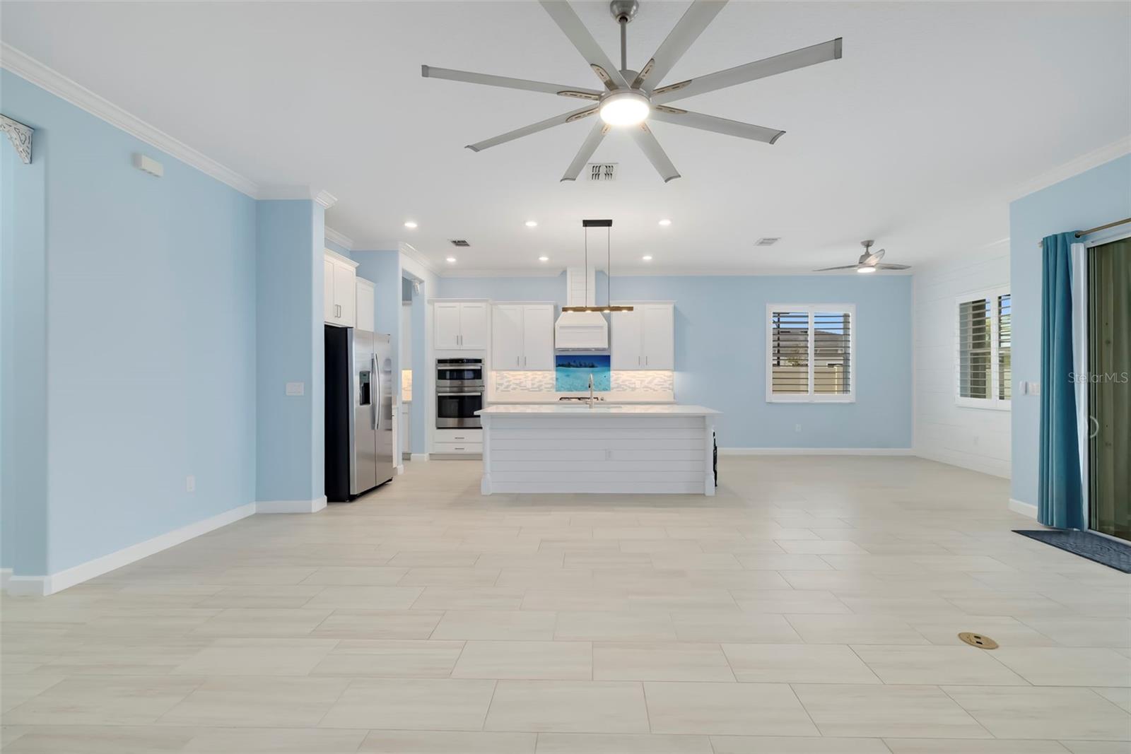 Open-plan kitchen with white island and cabinets, stainless steel appliances, and pale blue walls.