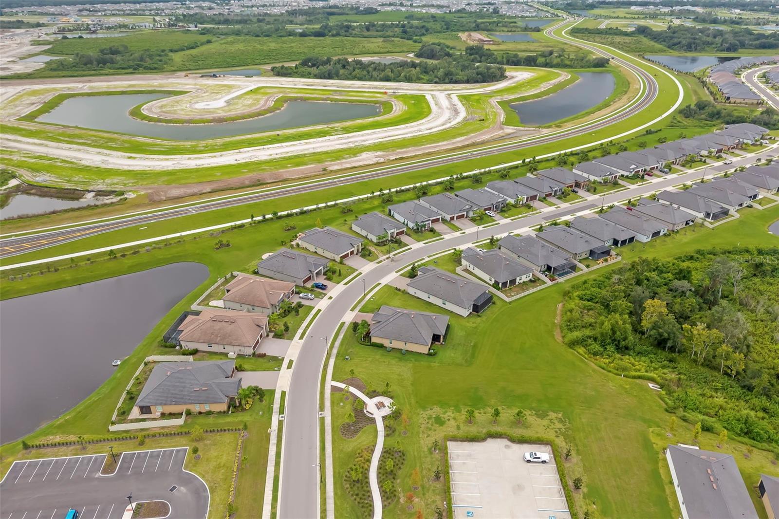 Aerial view of homes along a curving neighborhood street beside ponds and undeveloped land.
