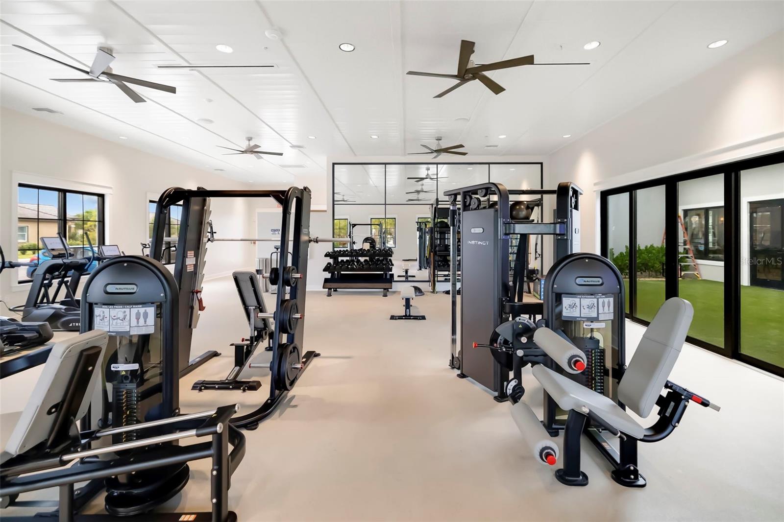 Fitness room with weight machines, treadmills, free weights, and large windows.