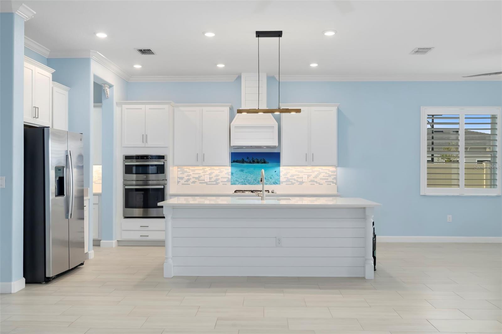 Kitchen with a large white island, stainless steel appliances, and a turquoise ocean-themed backsplash.
