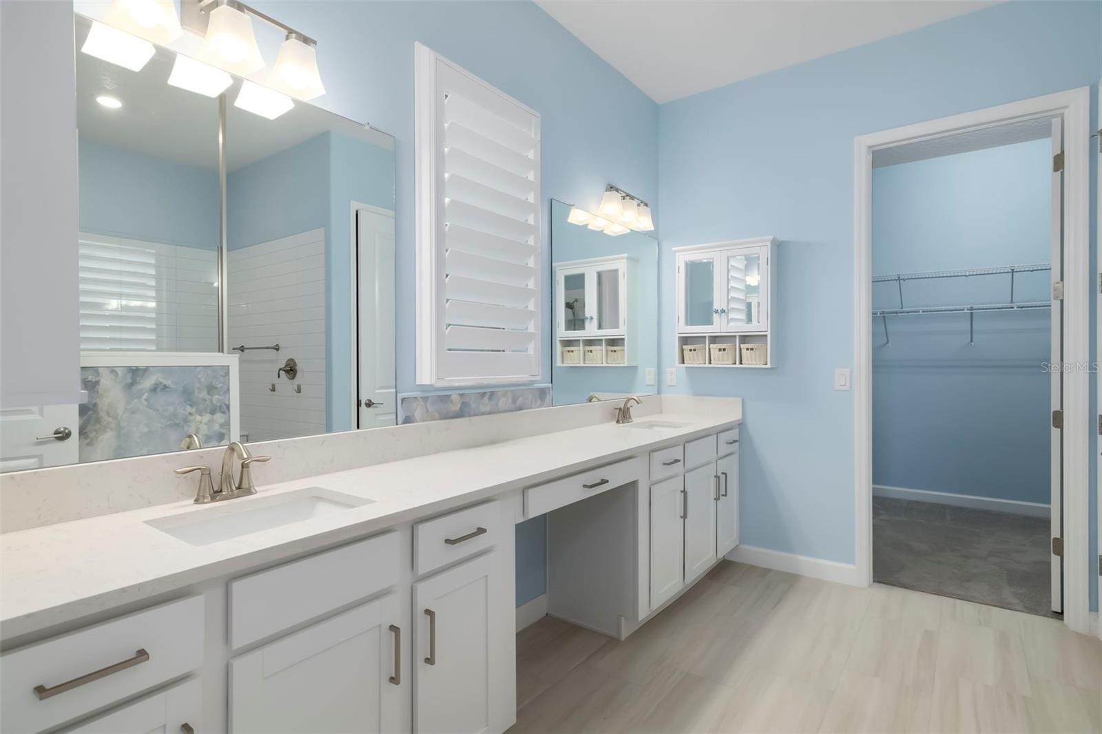 Bathroom with a long double-sink vanity and an open doorway to a walk-in closet.