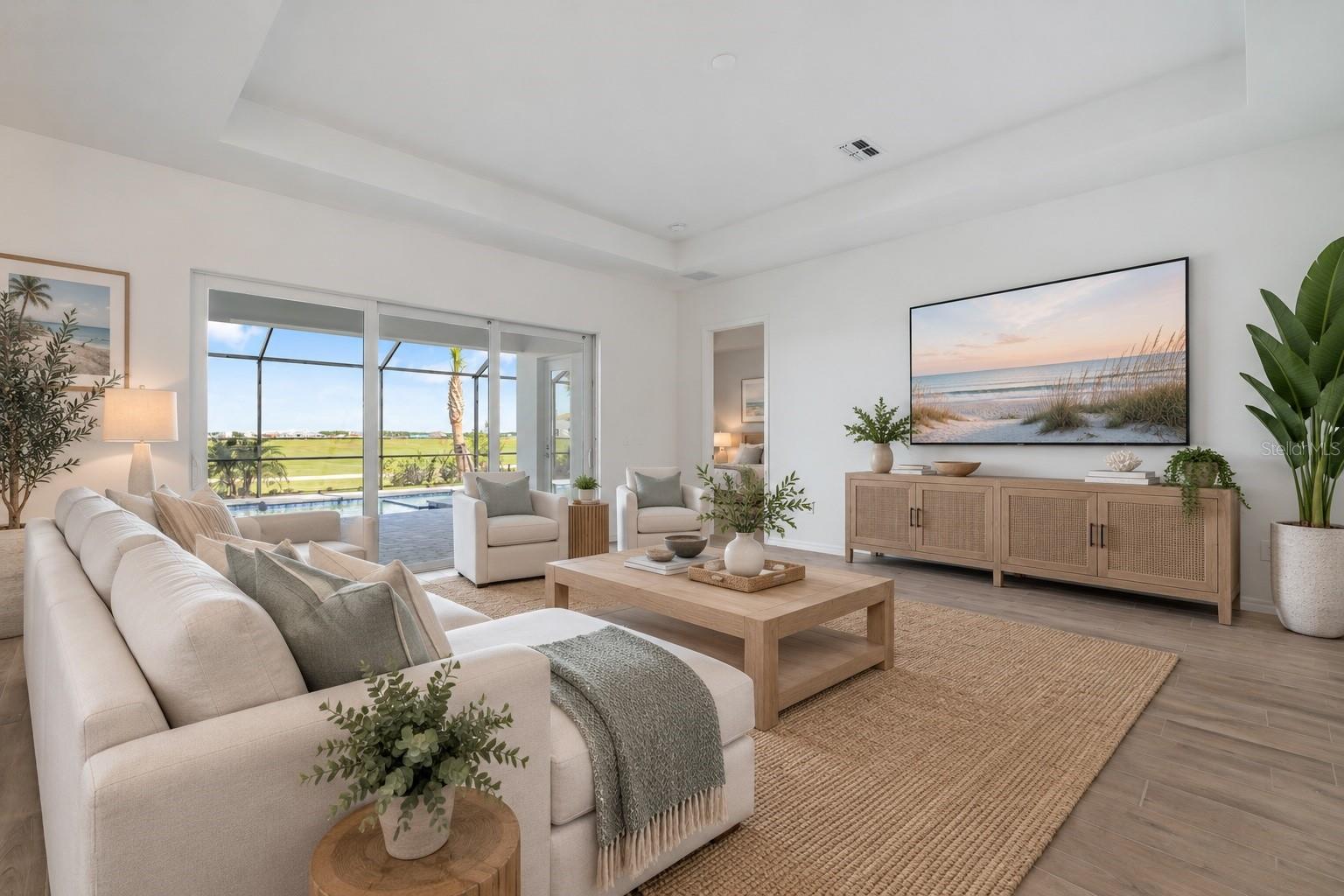Staged living room with a white sectional and large glass doors overlooking a screened patio, pool, and golf course.