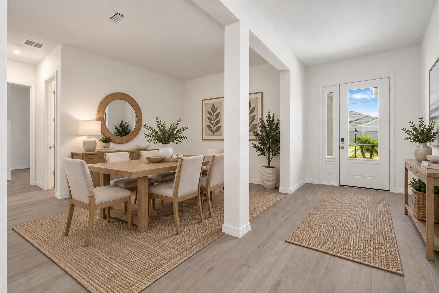Furnished dining room beside the entry foyer, with a wooden table, woven rugs, and a glass-paneled front door.