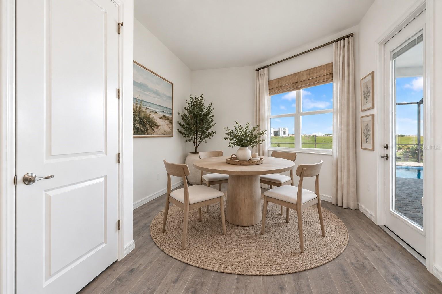 Dining room with a round wood table, woven rug, and glass door overlooking a pool.