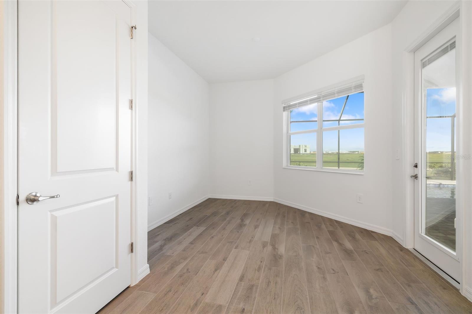 Empty room with wood-look flooring, a window, and a glass door overlooking a green open area.