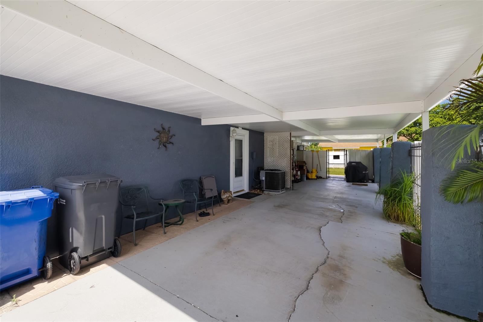 Covered carport with a long paved driveway, outdoor chairs, and a gated entrance.