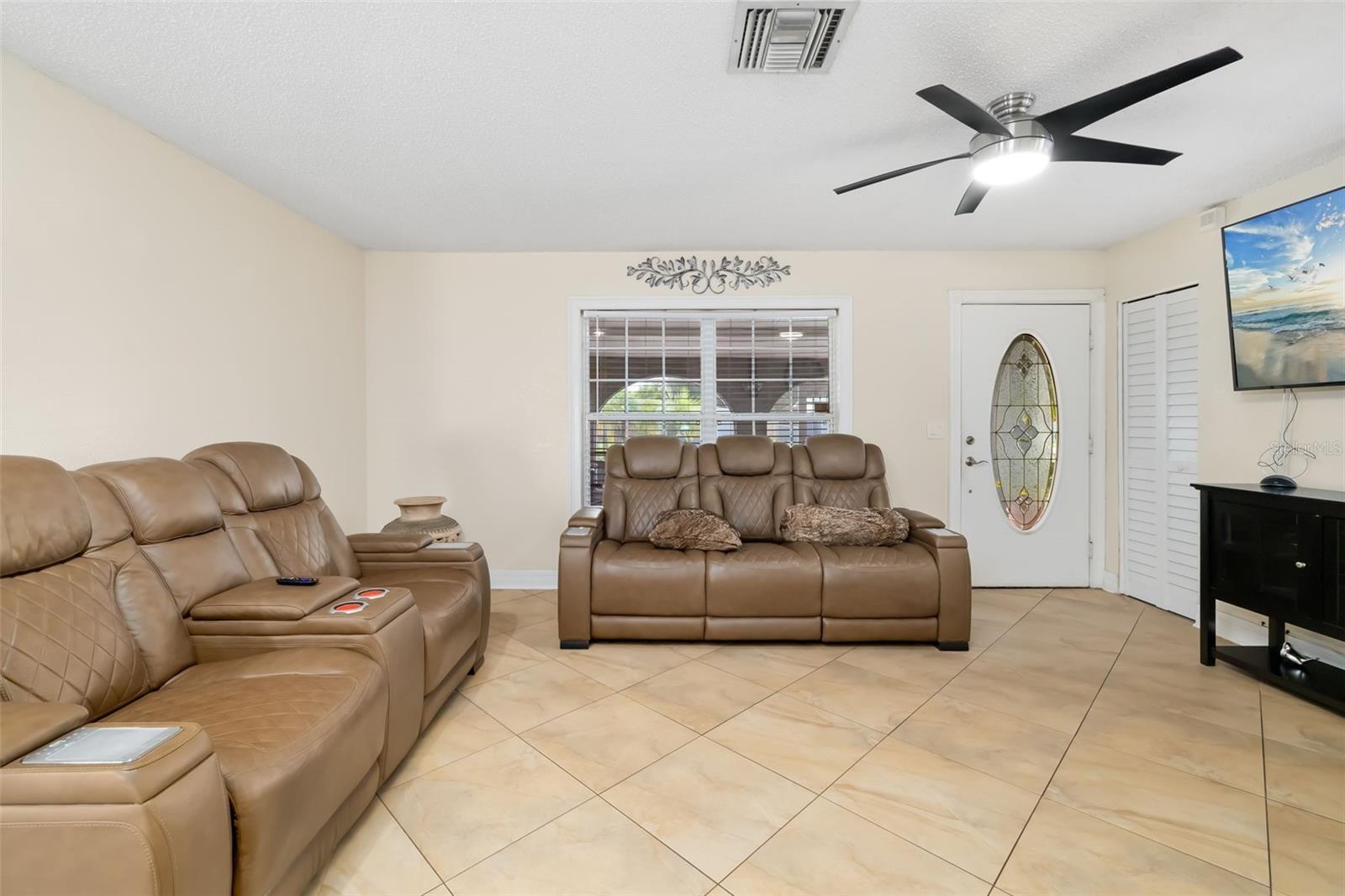 Living room with tan leather reclining sofas, beige tile floors, and a front door with oval glass.
