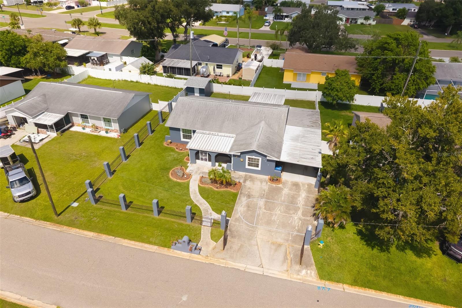 Aerial view of a gray single-story home with a fenced lawn and wide driveway.