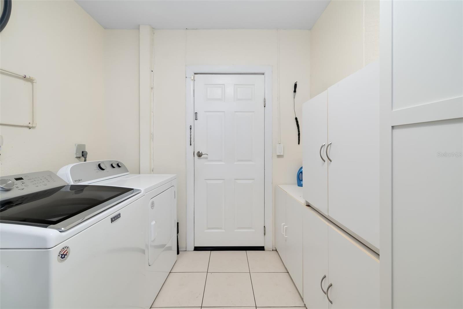 Laundry room with a white washer and dryer beside extensive white storage cabinets.