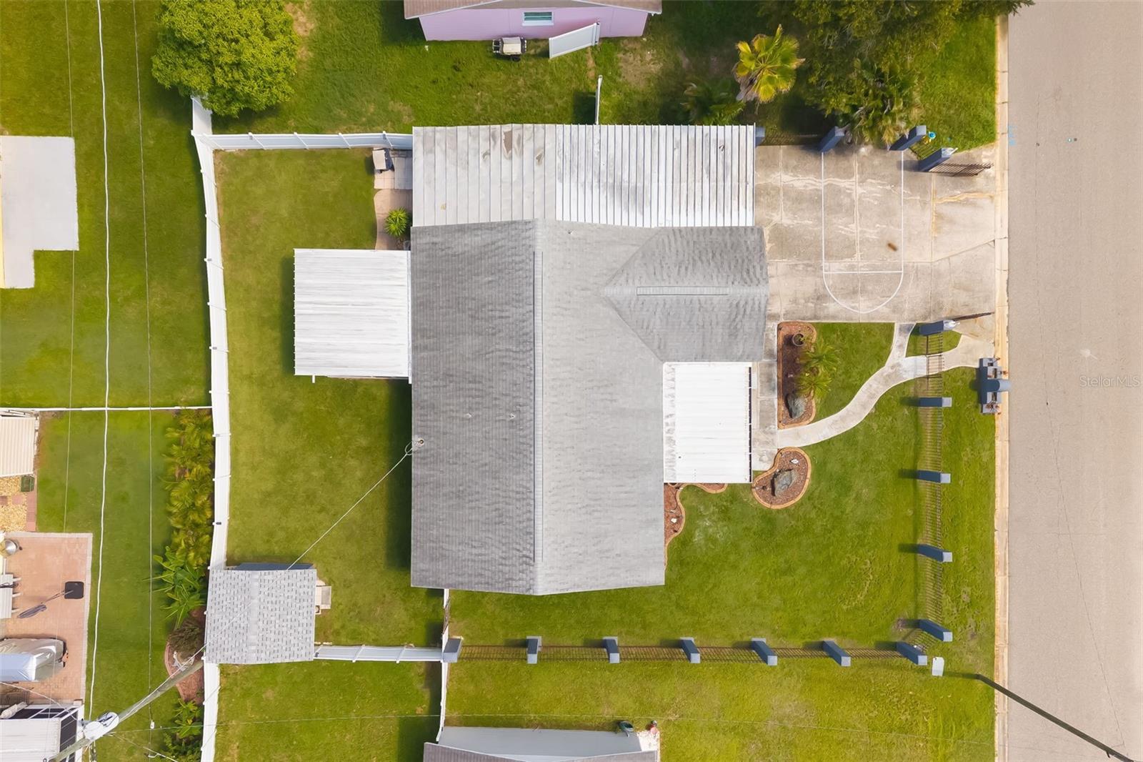Aerial view of a gray-roofed home with a fenced lawn, driveway, and curved front walkway.