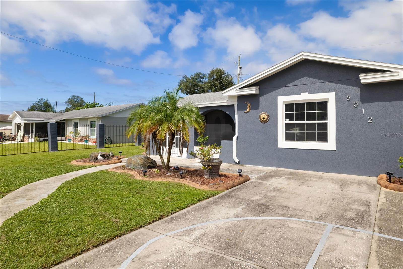 Gray single-story home with white trim, an arched entry, palm landscaping, and a curved driveway.