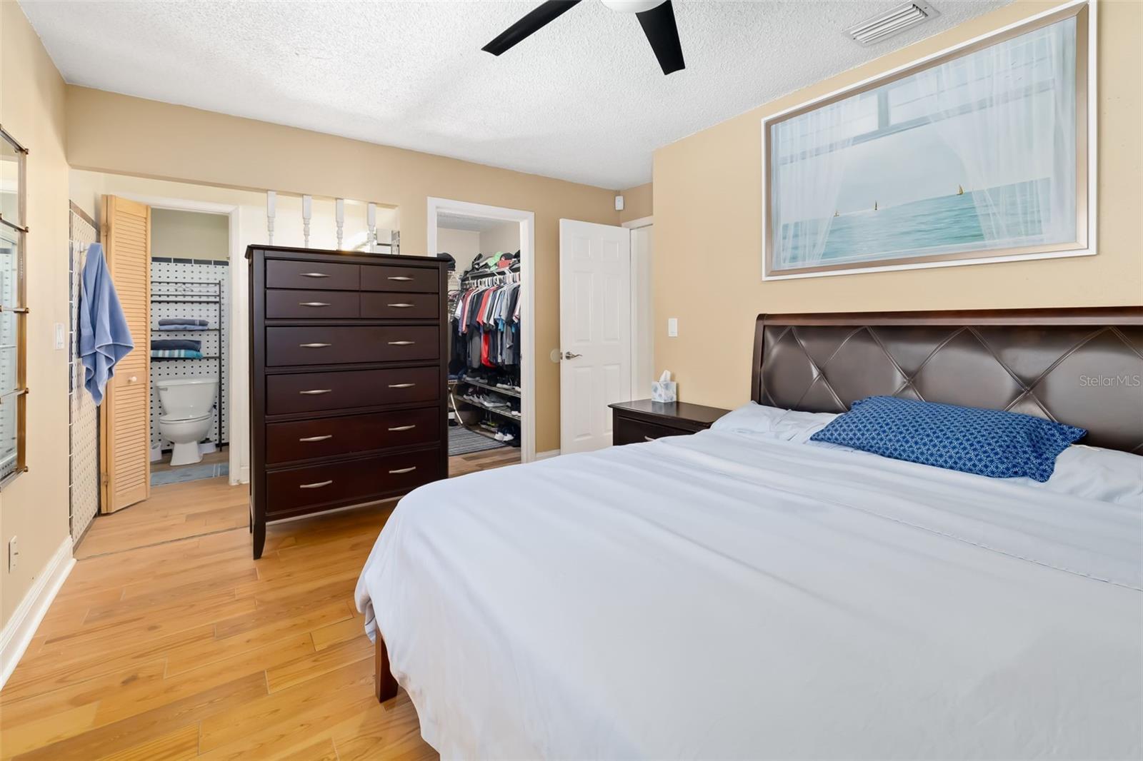 Bedroom with a large bed, hardwood floors, and open doorways to a closet and bathroom.