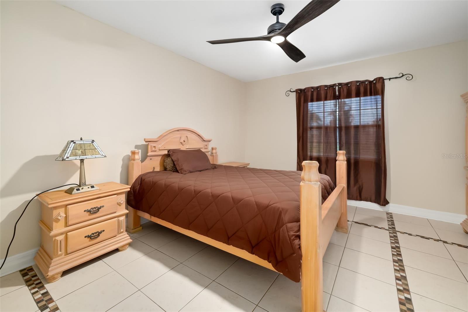 Bedroom with a light wood four-poster bed, brown bedding, tiled floor, and curtained window.