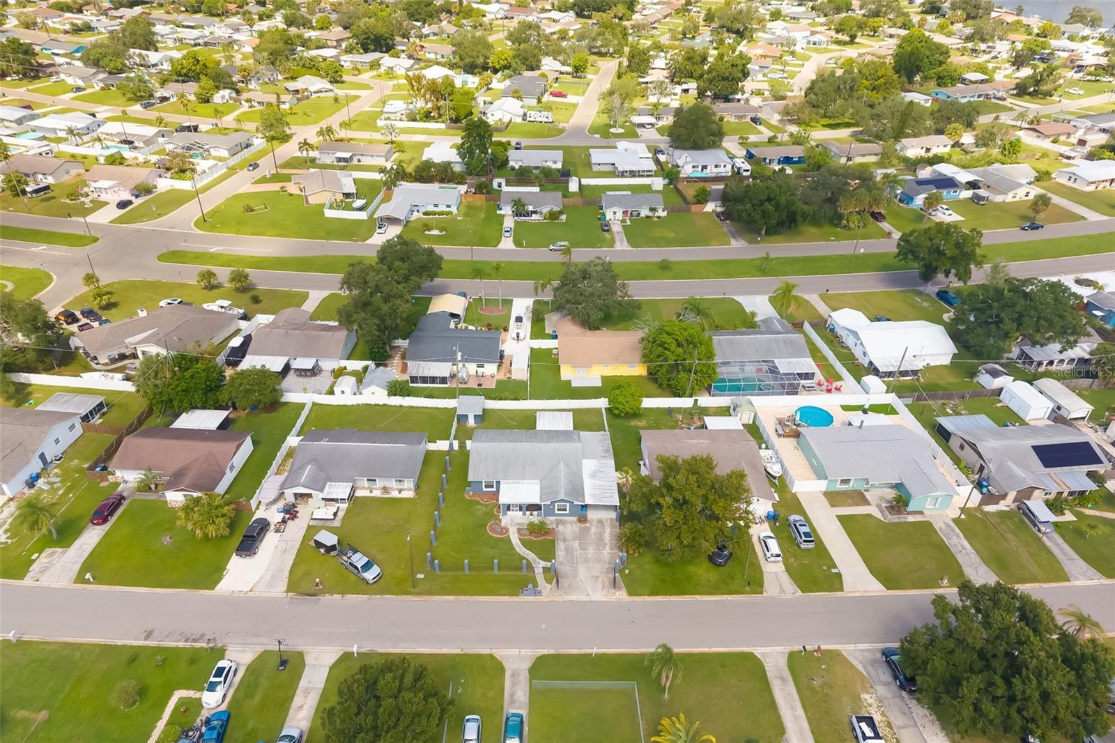 Aerial view of a residential neighborhood with detached homes, green yards, and a screened pool.