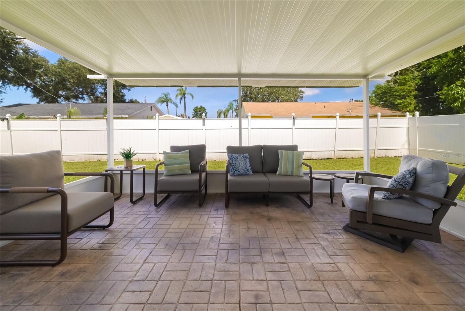 Covered patio with gray seating, stamped pavers, and a fenced backyard.