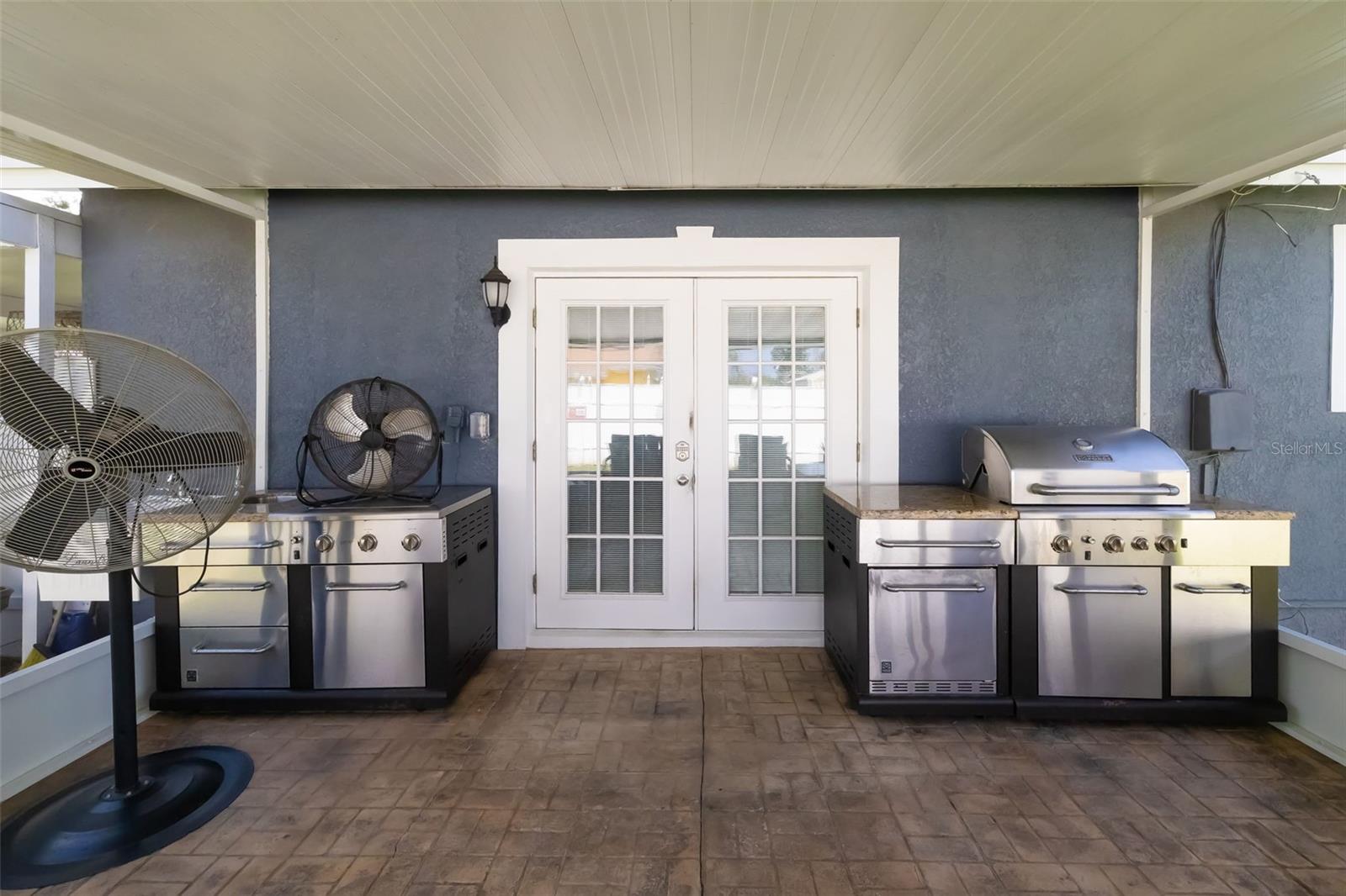 Covered patio with stainless steel outdoor kitchens and grills beside white French doors.