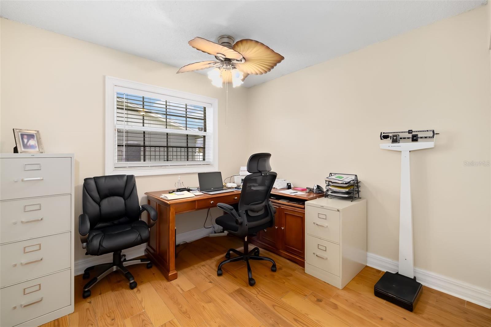 Furnished home office with a corner desk, black chairs, filing cabinets, and hardwood flooring.