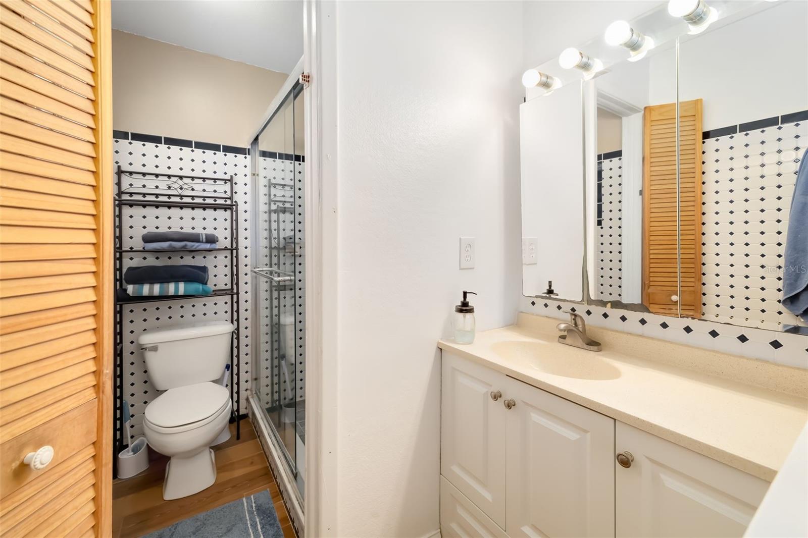 Bathroom with a white vanity, illuminated mirror, glass shower, and black-and-white patterned tile.
