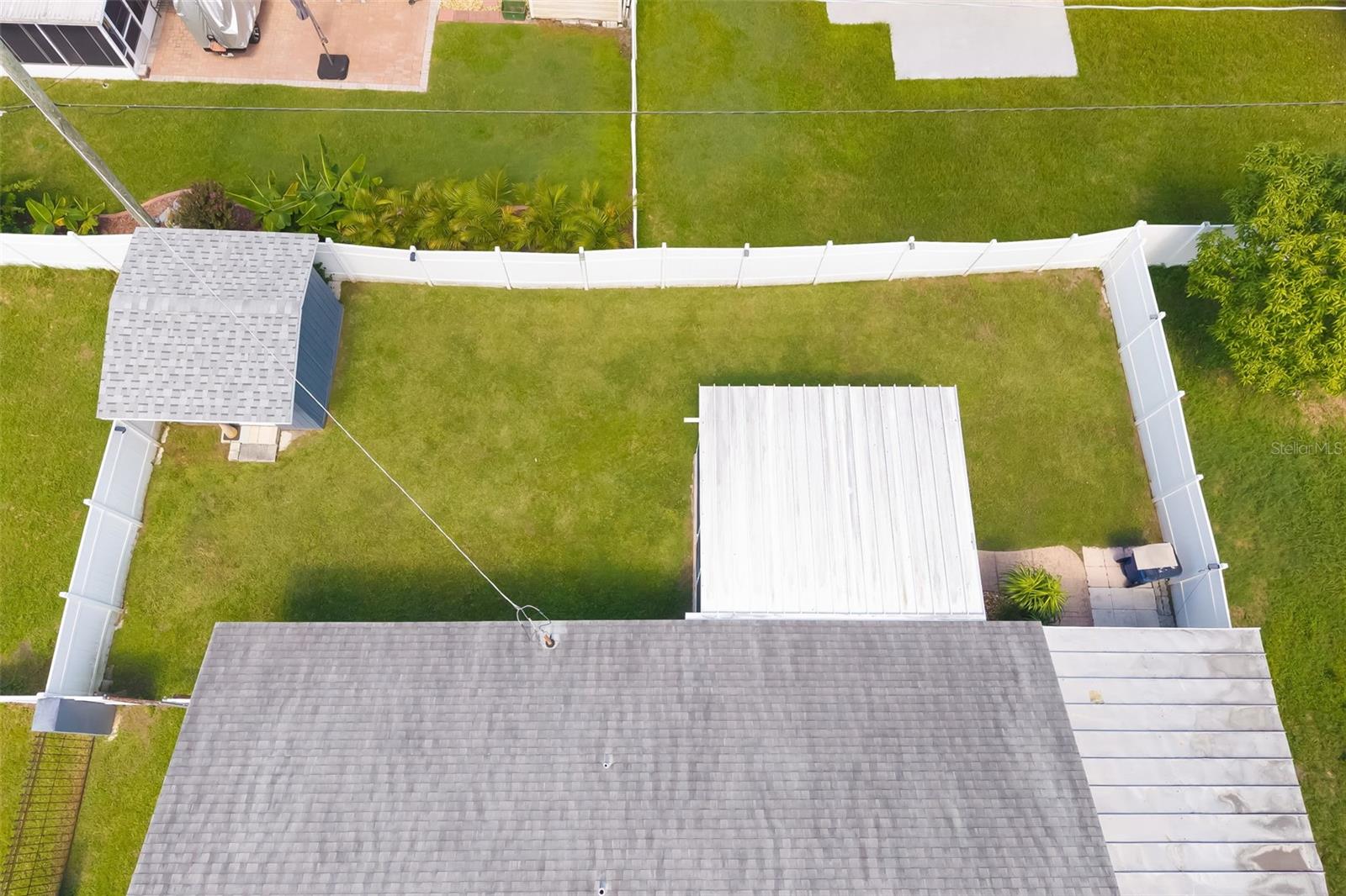 Aerial view of a fenced backyard with a large lawn, small shed, and patio areas.