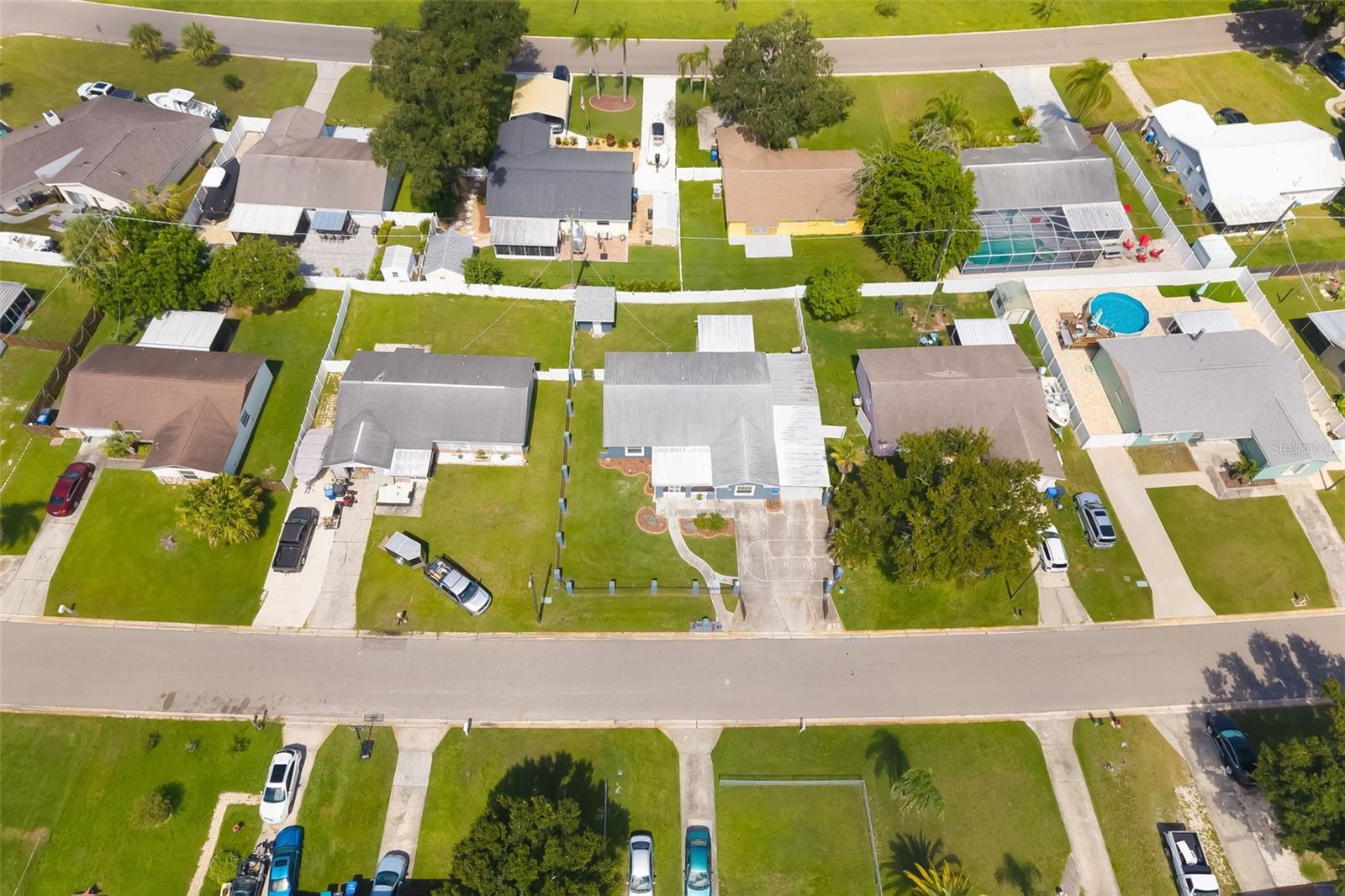 Aerial view of a residential block with fenced yards, green lawns, and a screened pool enclosure.