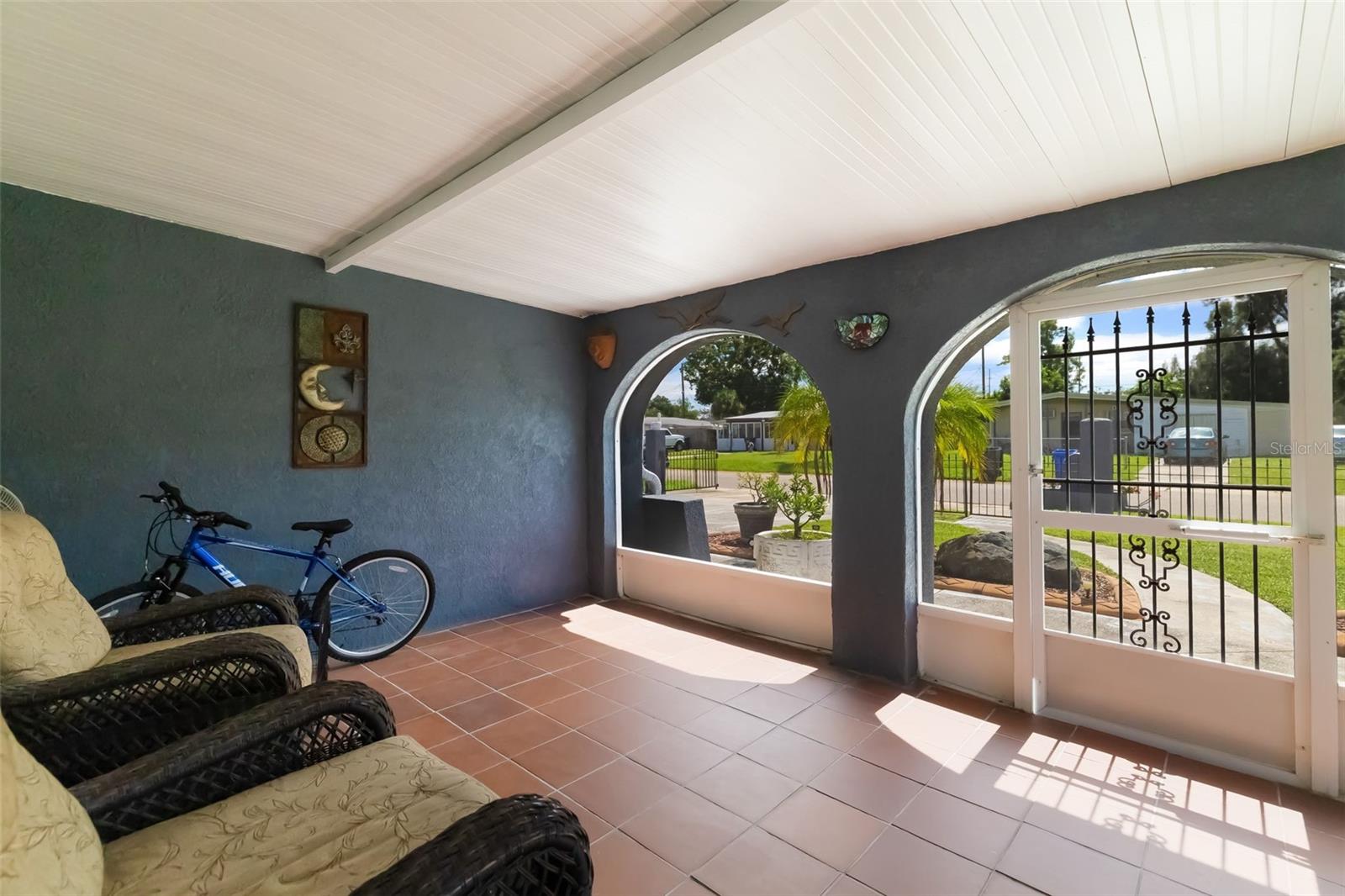 Covered porch with arched openings, wicker chairs, tiled floor, and decorative metal security gate.
