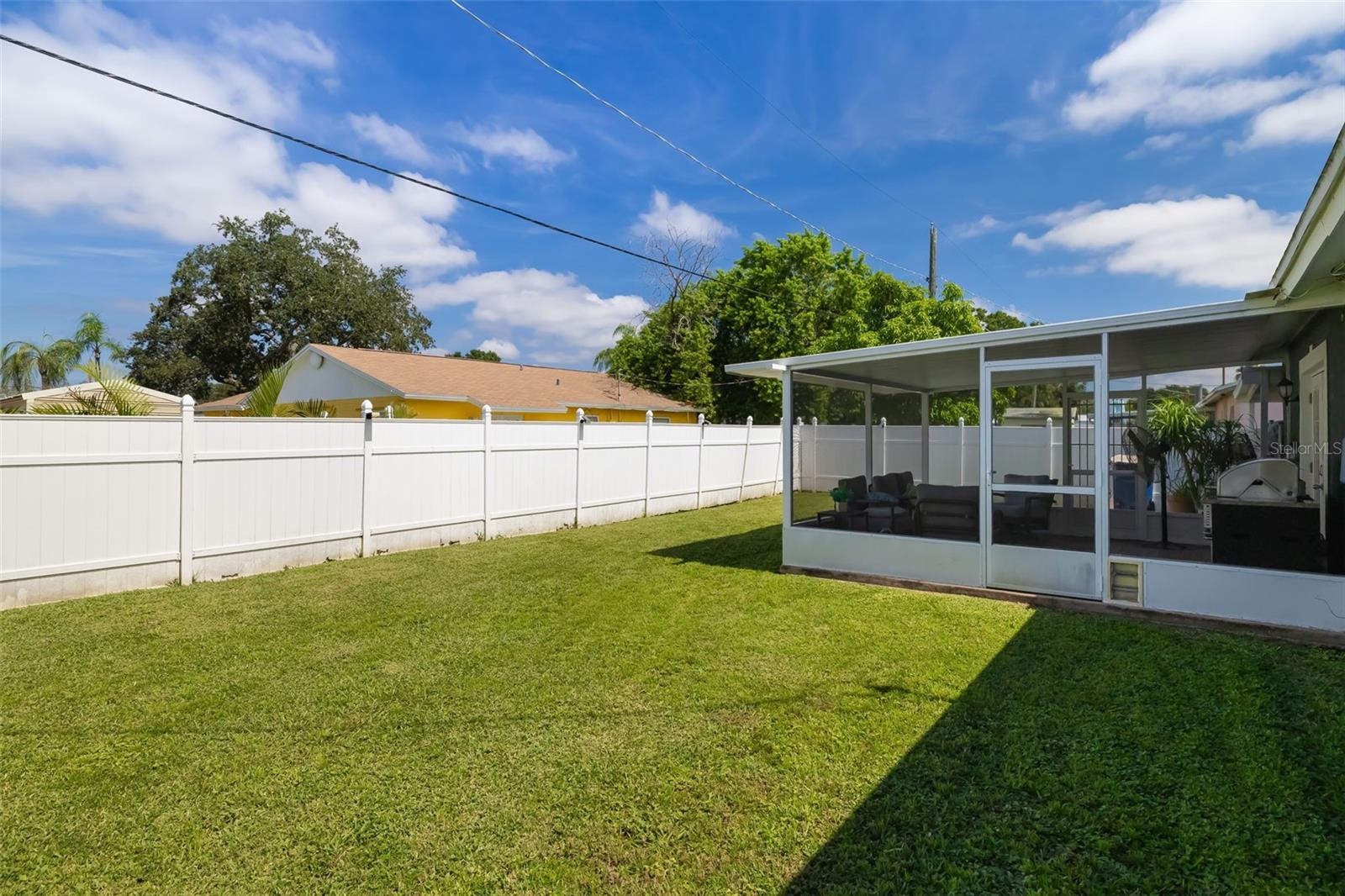Fenced backyard with a broad lawn and screened patio with outdoor seating.