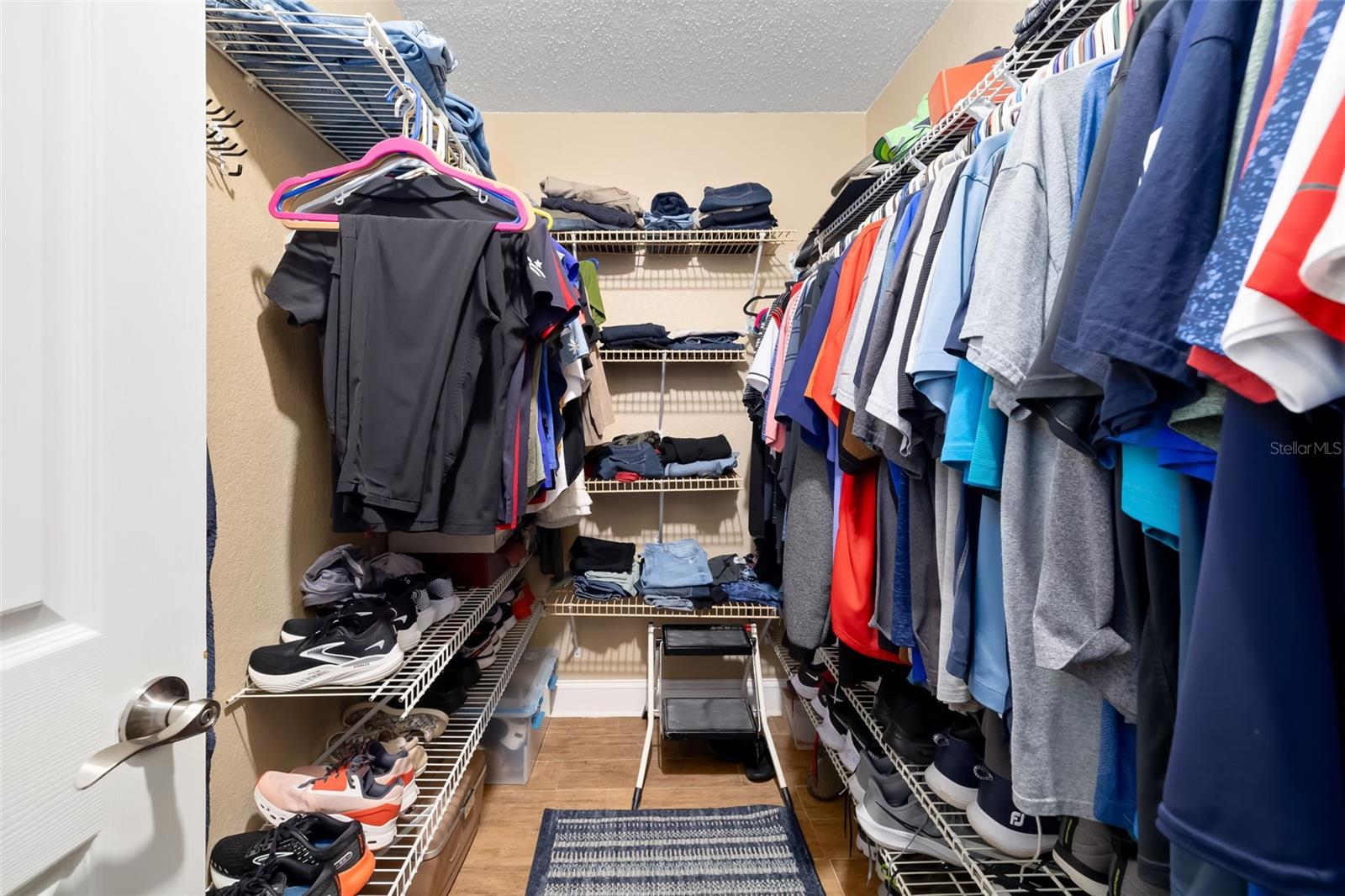 Walk-in closet with clothes on both sides, shoe shelves, and a step stool.