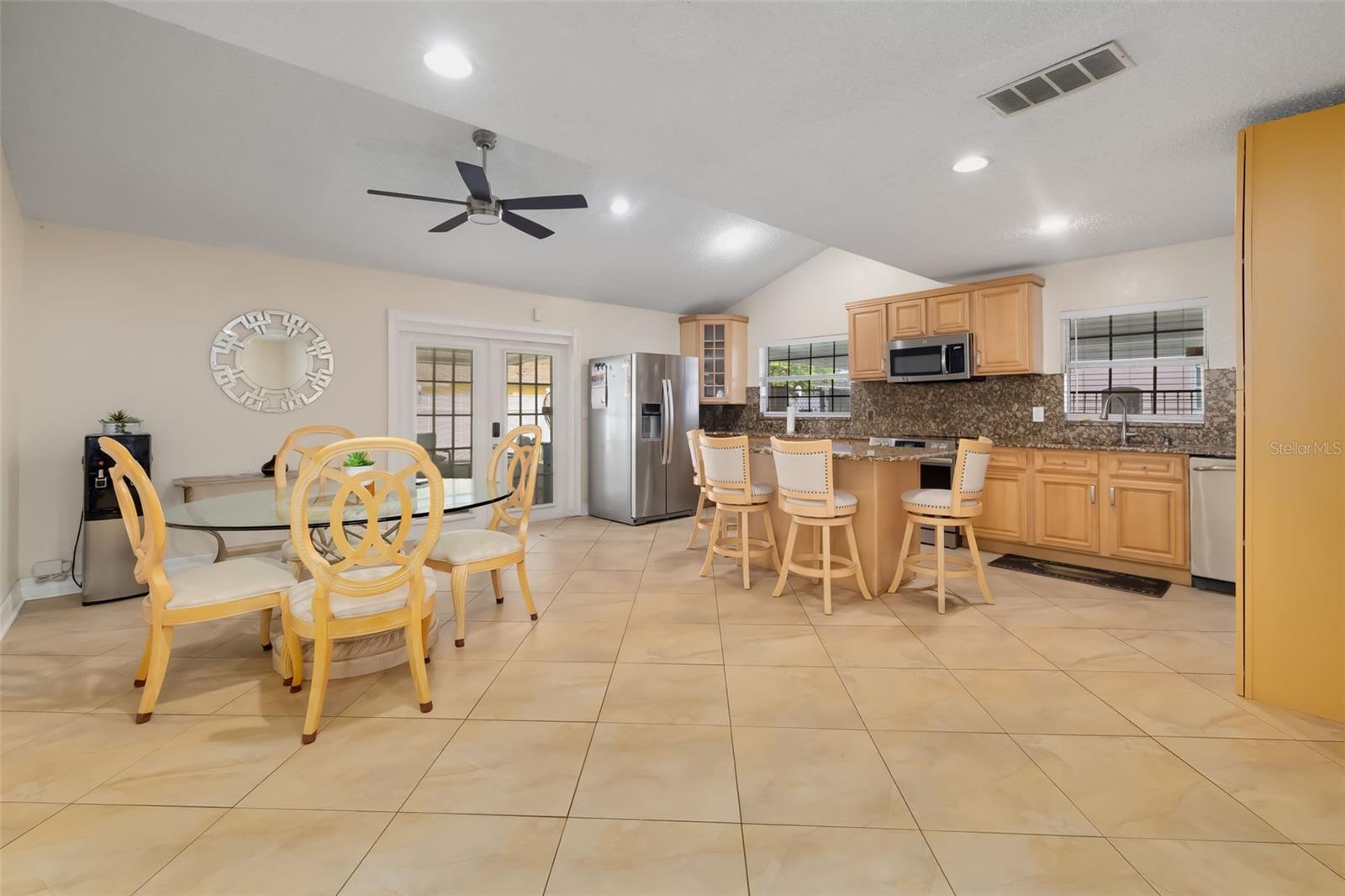Kitchen and dining area with wood cabinets, stainless steel appliances, breakfast bar, and glass table with yellow chairs.