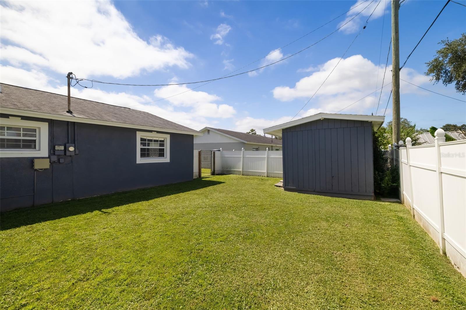 Fenced backyard with a broad lawn, detached storage shed, and side of the home.