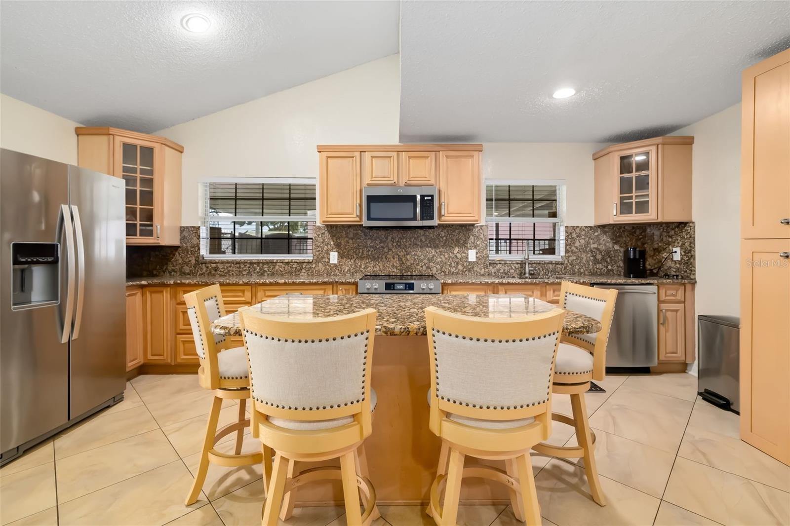 Kitchen with wood cabinetry, stainless steel appliances, and a large island with four bar stools.