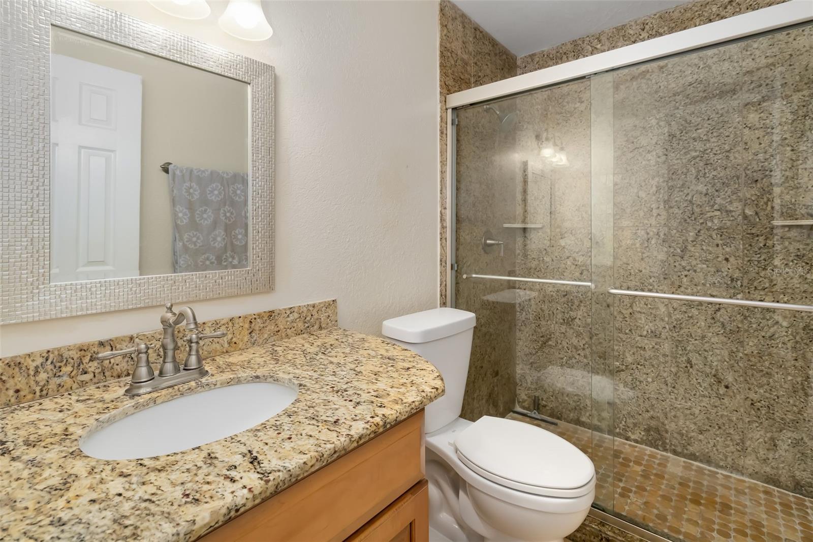 Bathroom with a granite vanity, framed mirror, and glass-enclosed tiled shower.