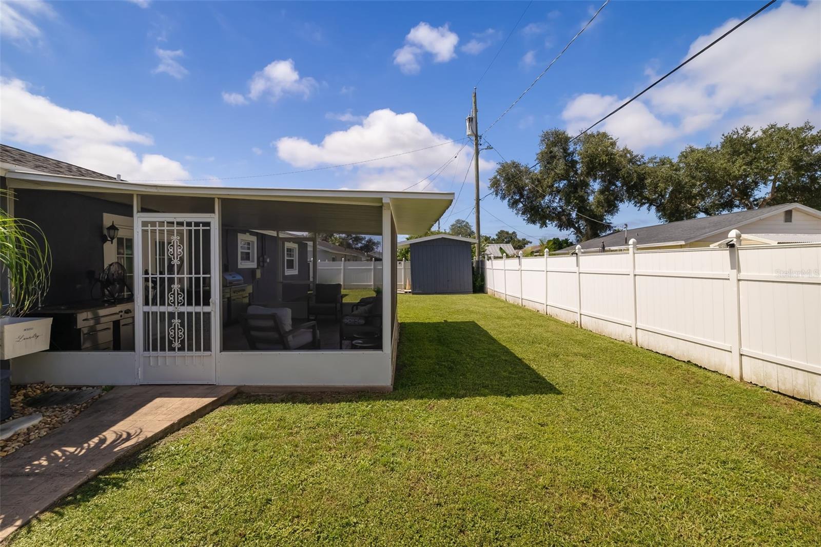Backyard with a spacious lawn, white privacy fence, and covered screened patio.