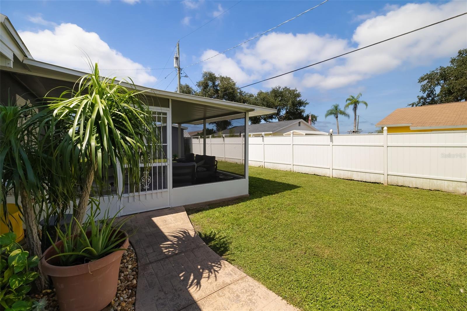 Backyard lawn beside a covered screened patio, white privacy fence, and paved walkway.