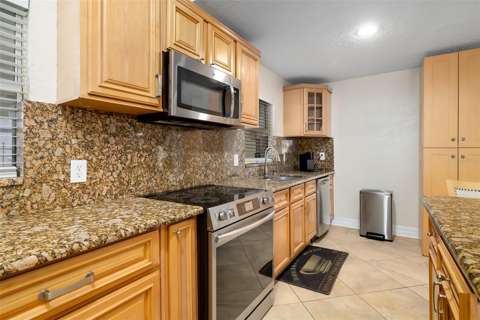 Kitchen with honey-colored cabinets, patterned stone counters and backsplash, and stainless steel appliances.