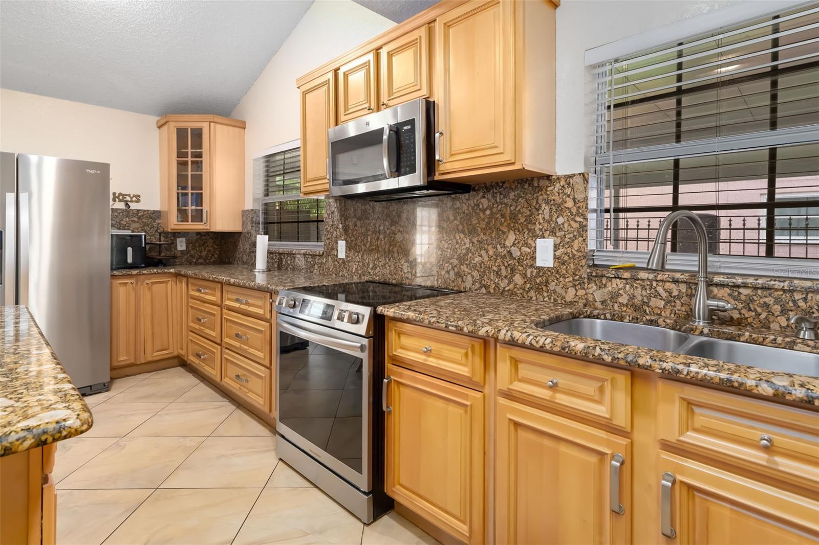 Kitchen with honey-colored cabinets, stone countertops, stainless steel appliances, and a double-basin sink.