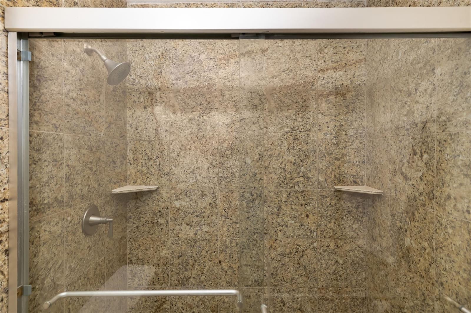 Walk-in shower with stone-look tile, glass enclosure, and built-in corner shelves.