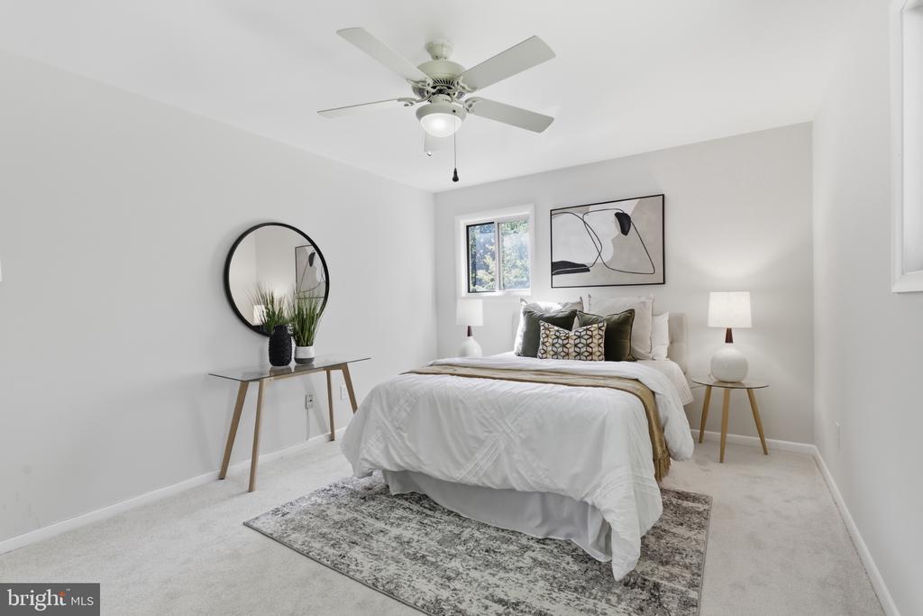 Staged bedroom with a white bed, ceiling fan, round mirror, and gray area rug.