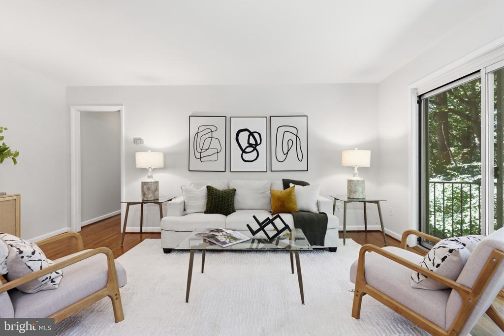Staged living room with a white sofa, abstract wall art, and a large window overlooking trees.