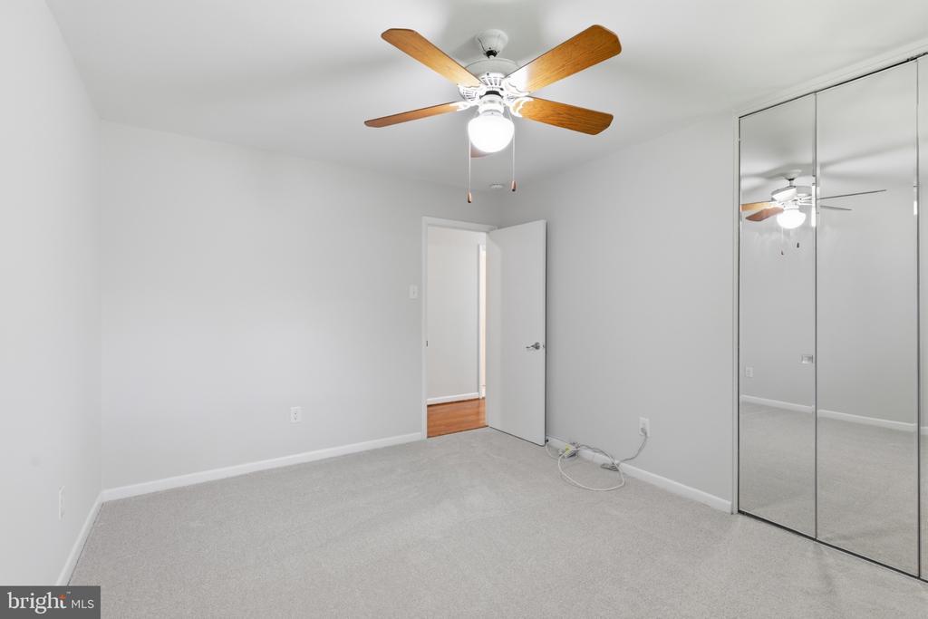 Empty bedroom with mirrored closet doors, light gray carpet, and a ceiling fan.
